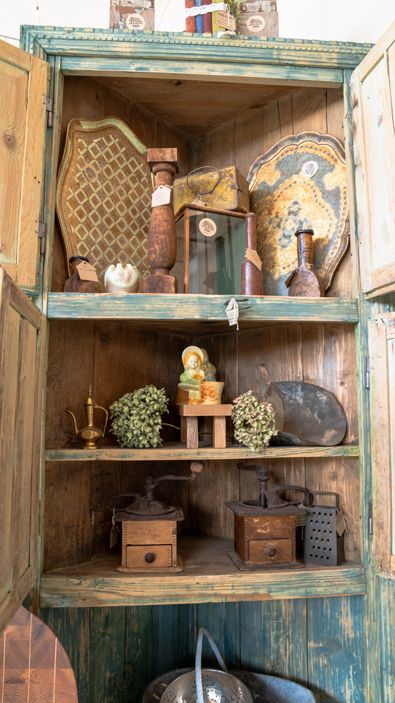 Open green cupboard filled with pottery and small antiques