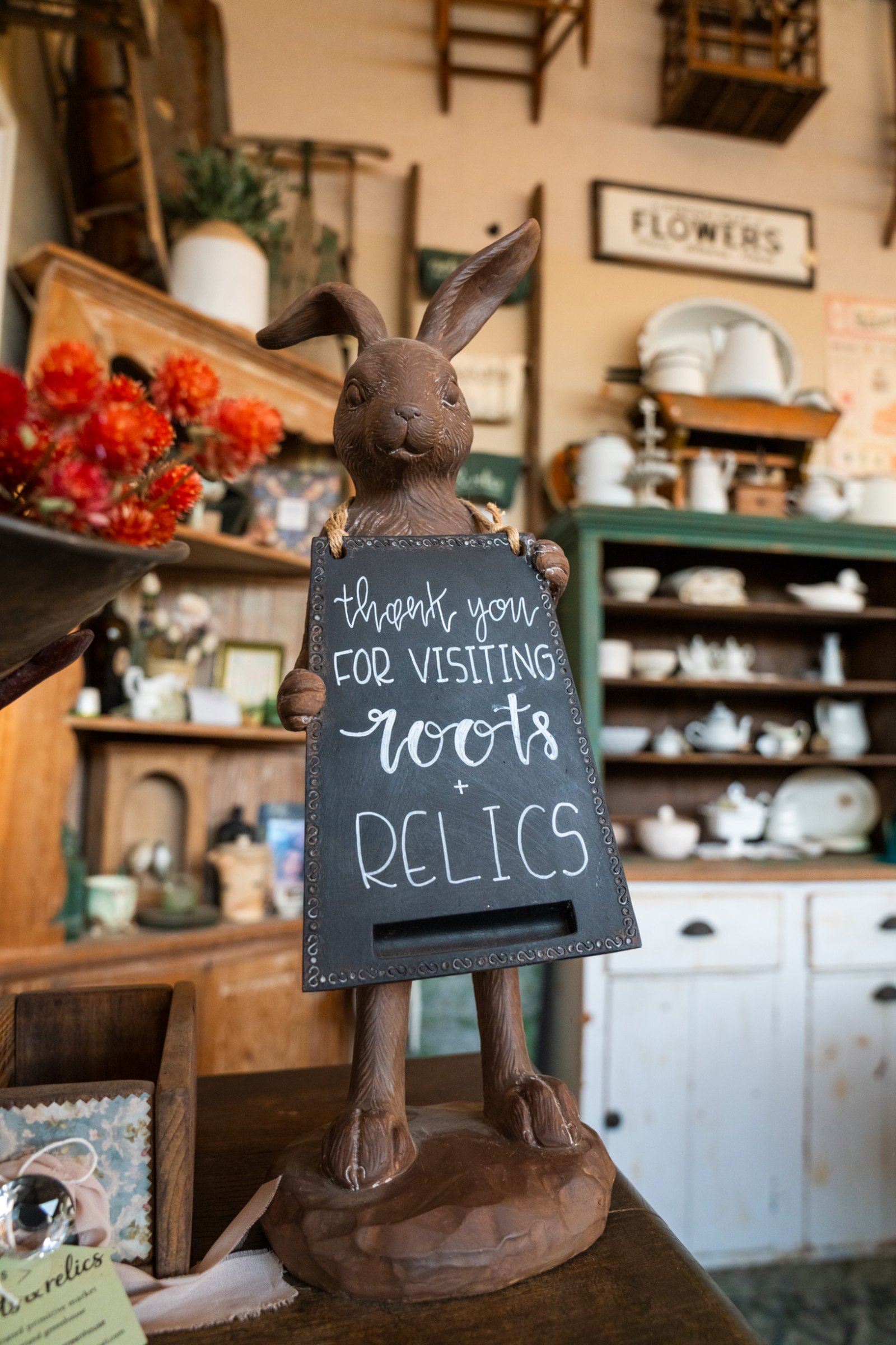 A rabbit figure holding a handwritten thank-you sign inside the Roots and Relics greenhouse