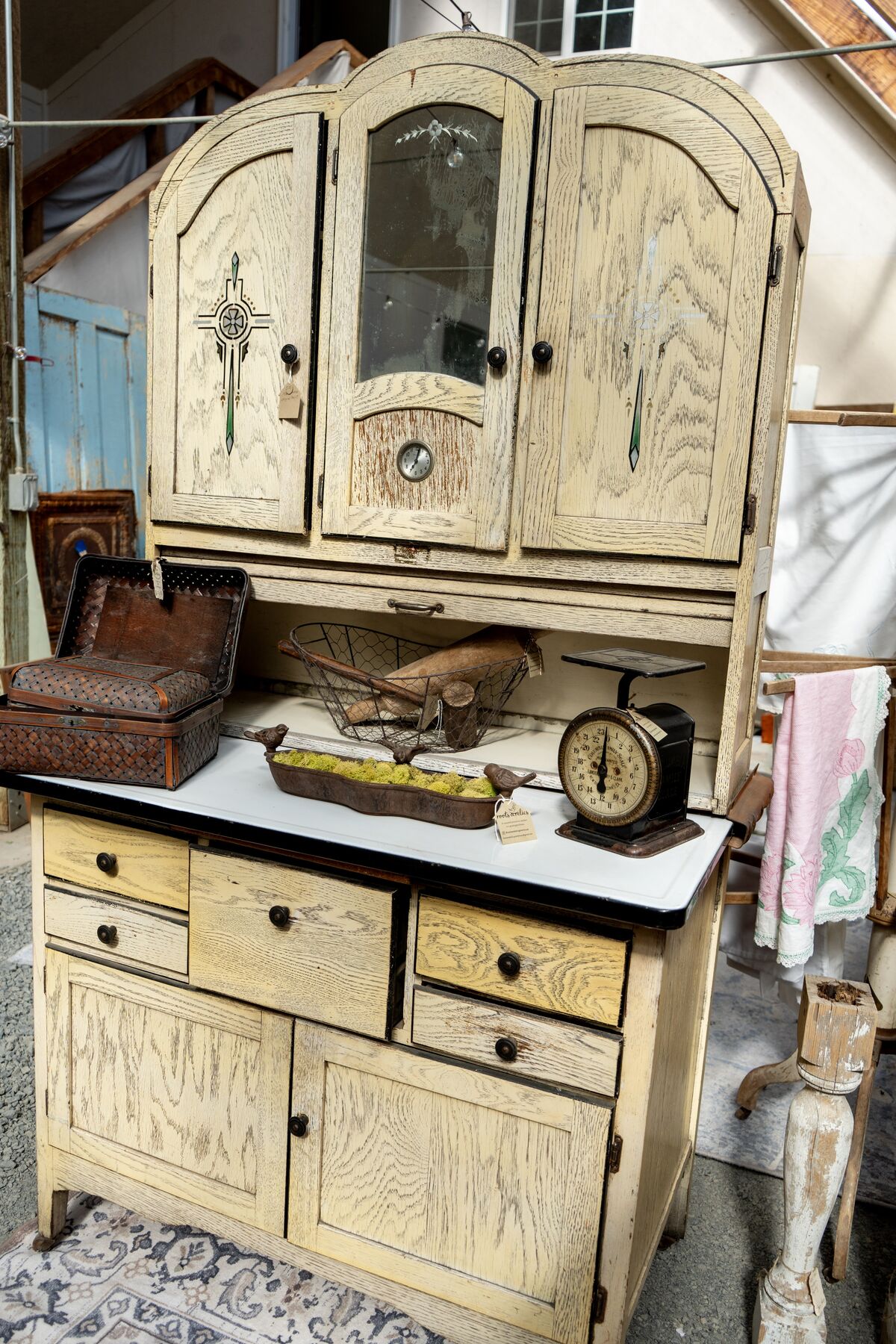 A painted antique cupboard arranged with a scale, basket, and gathered pieces