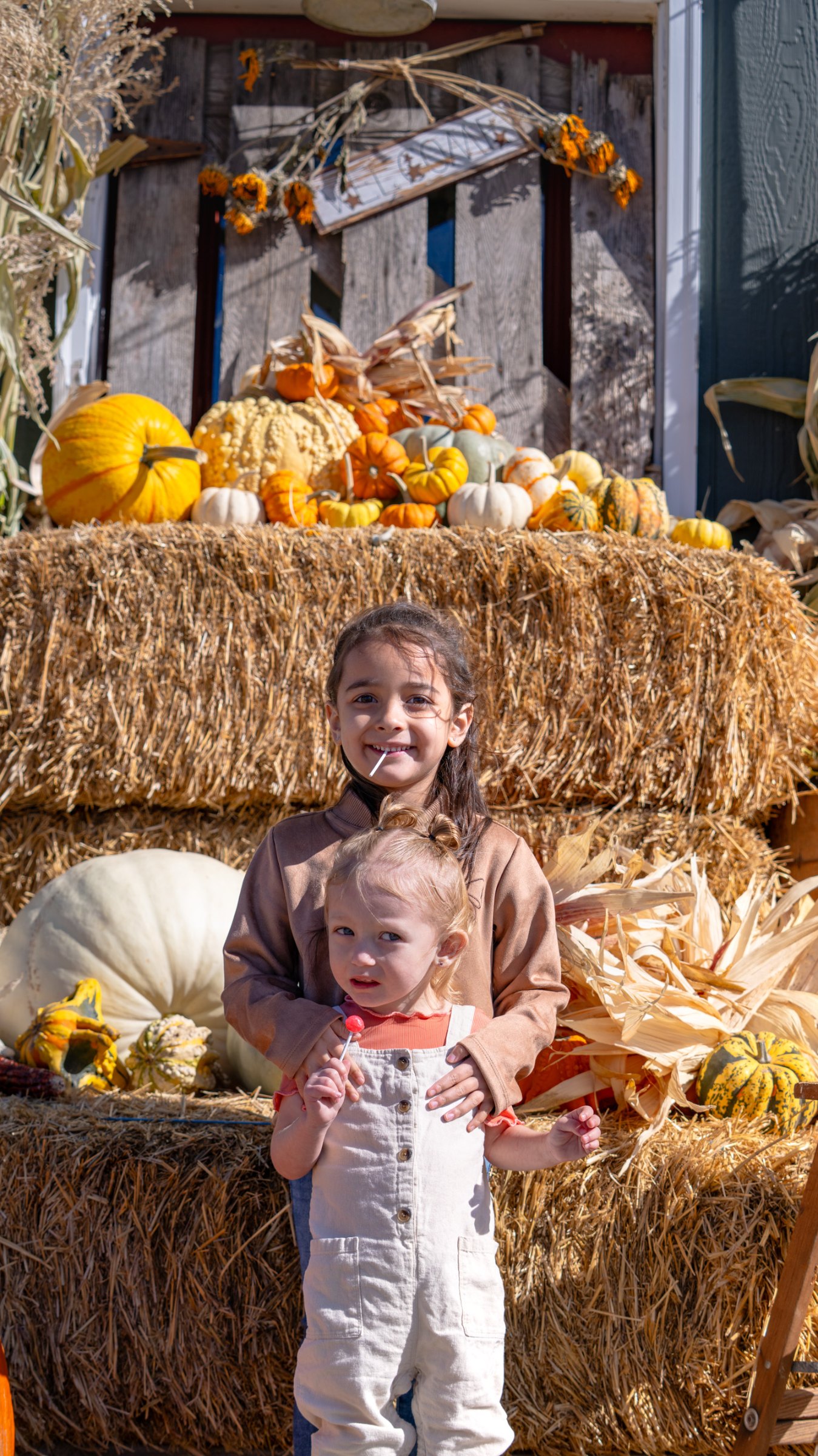 Two children posing beside pumpkins and straw bales
