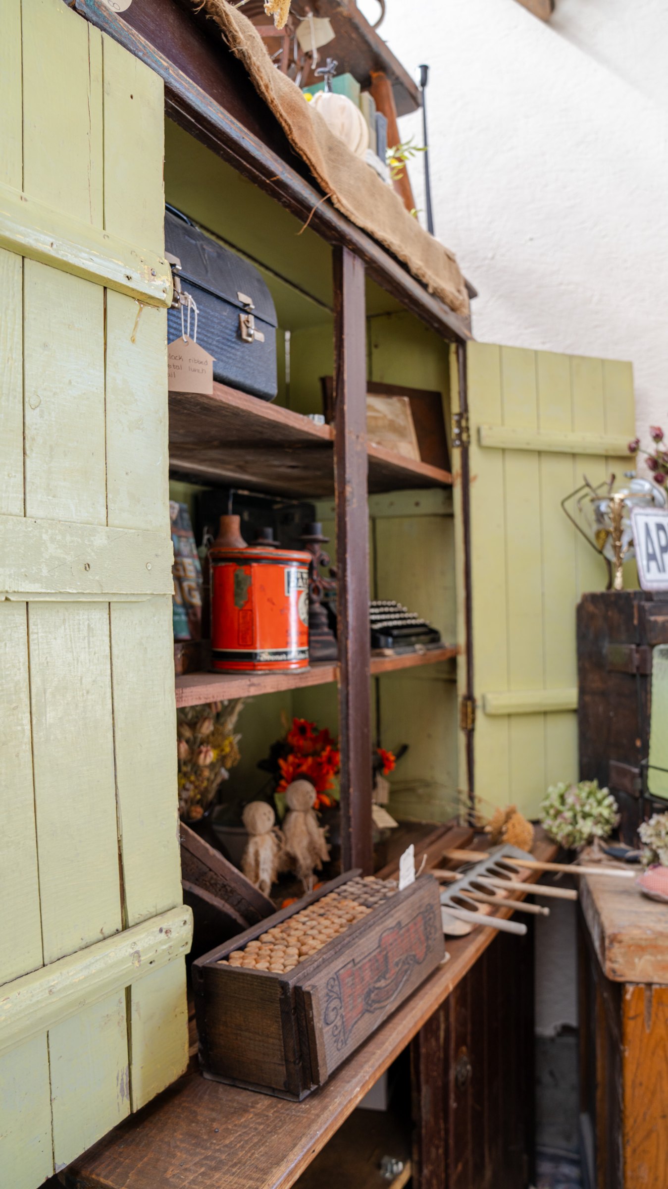 Open green cabinet displaying tins and vintage household pieces