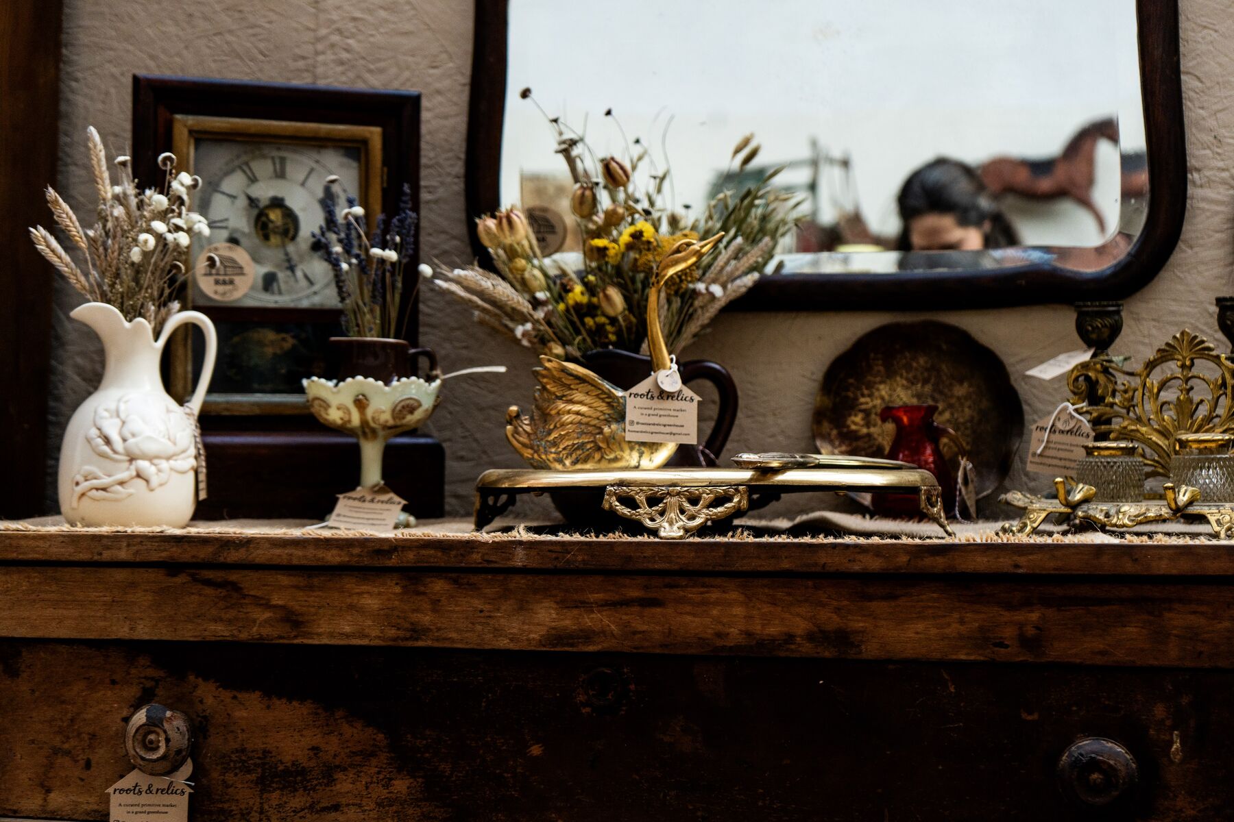 An antique clock, dried botanicals, and a brass swan arranged in a greenhouse vignette