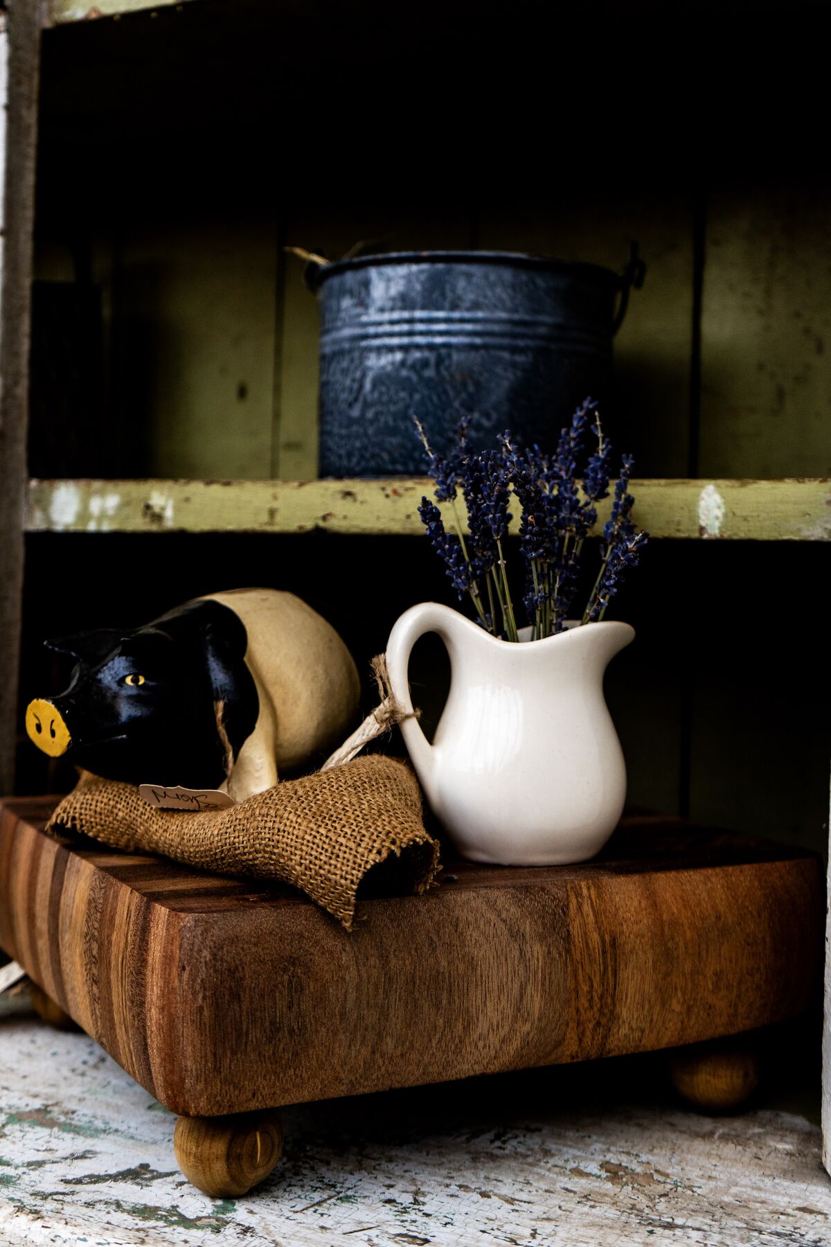 A gathered lavender bundle, ironstone pitcher, and primitive pig in a rustic cupboard