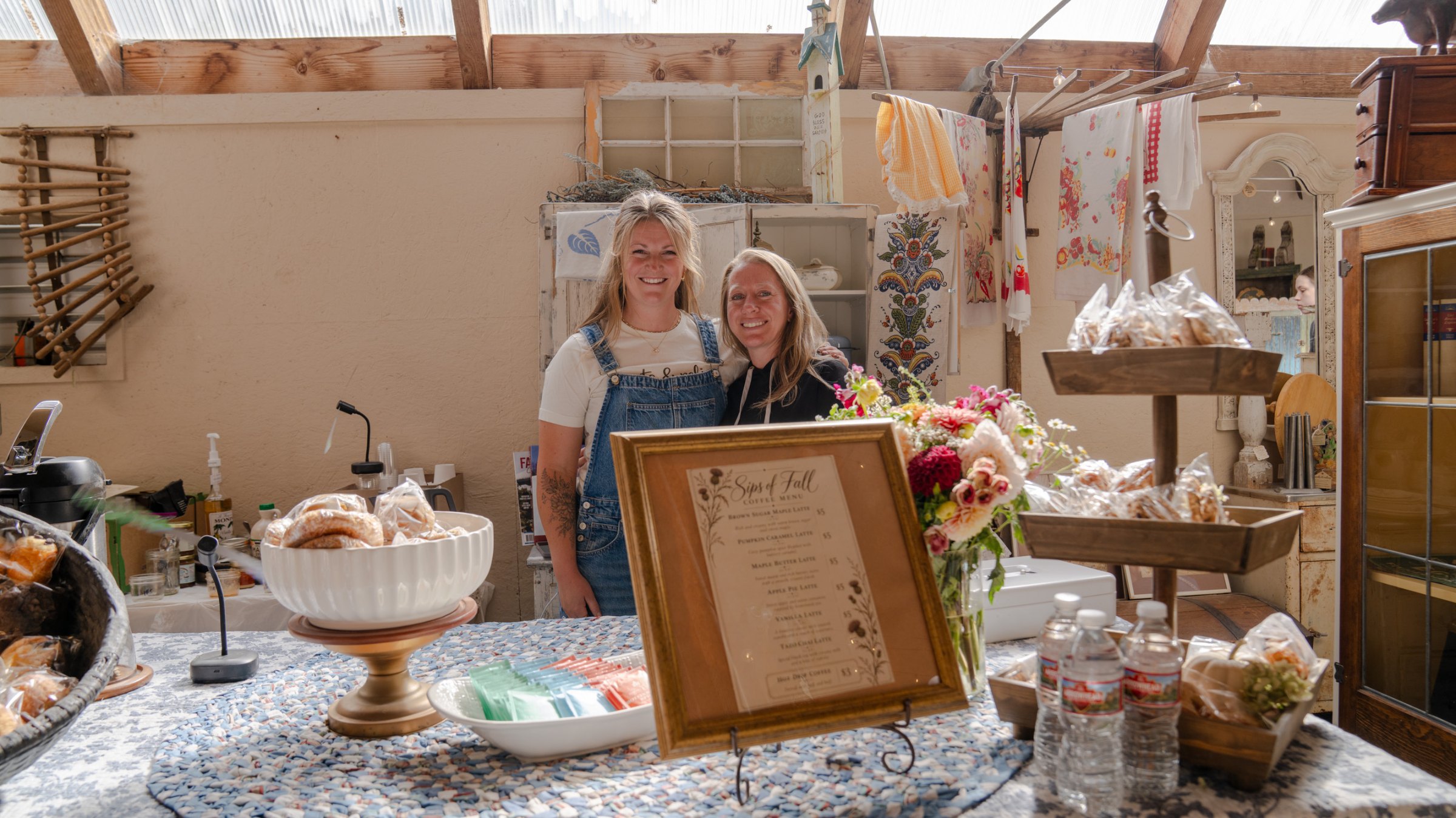 Two people behind a table of cakes, flowers, and vintage serving pieces