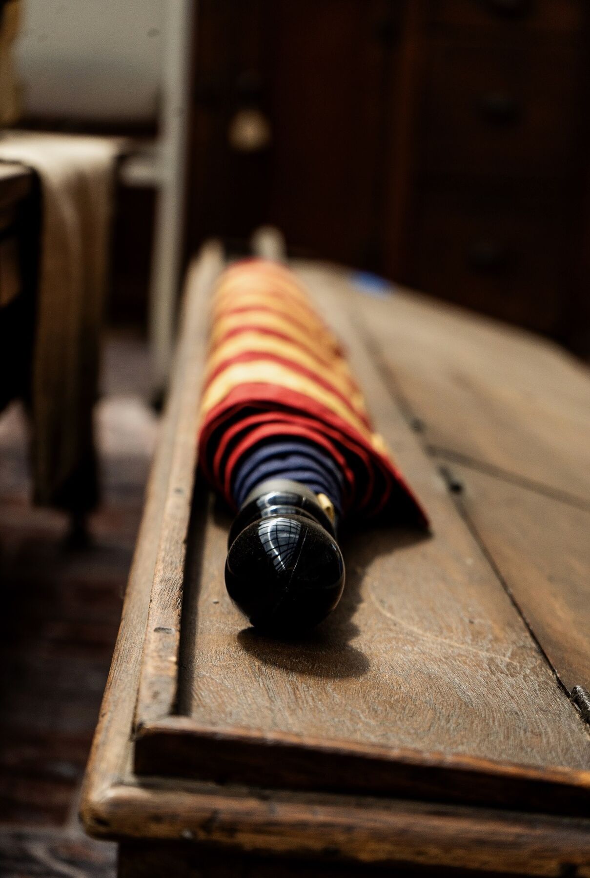 A red and gold striped vintage umbrella resting on an antique wooden surface